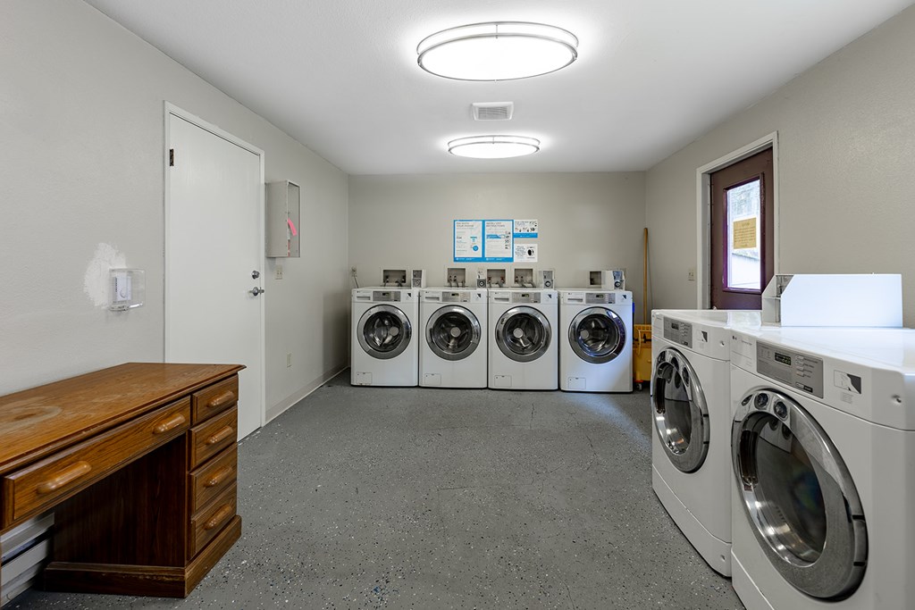 A laundry room with a row of washing machines and a wooden cabinet.