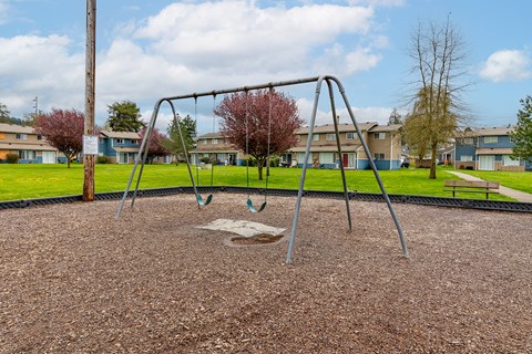 A playground with a swing set in the foreground and apartment buildings in the background.