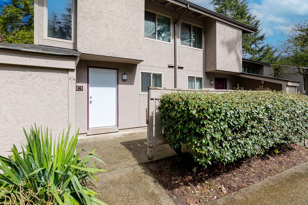 A building with a red door and windows with bushes in front.