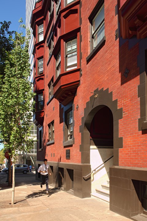 A man is walking on a sidewalk next to a red brick building.