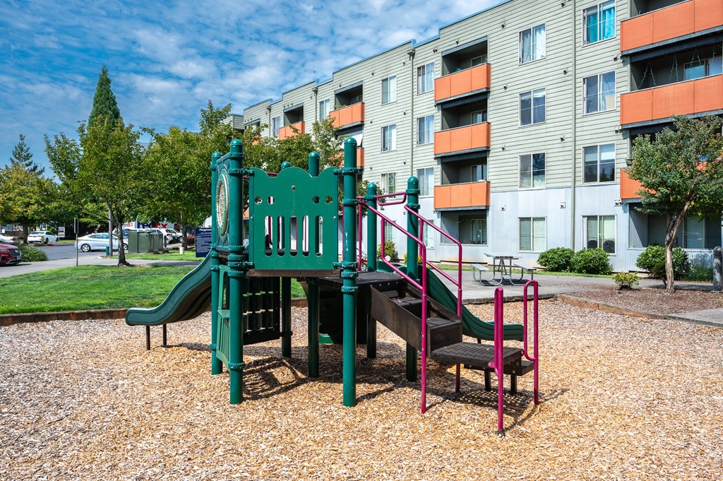 A playground with a green slide and a red swing set.