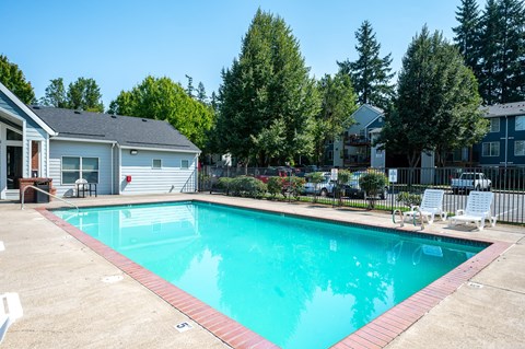 A swimming pool surrounded by a concrete patio and a black fence.