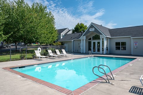 A pool with a diving board and lounge chairs in front of a building.