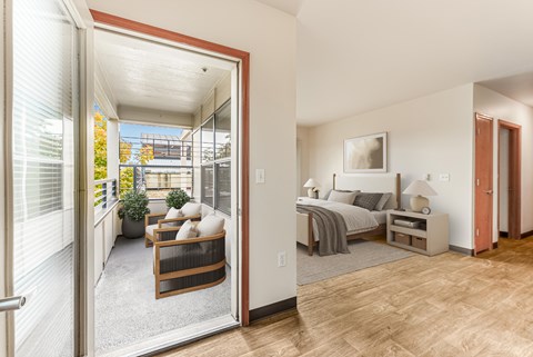 A bedroom with a bed, nightstand, and chair is shown through an open door.