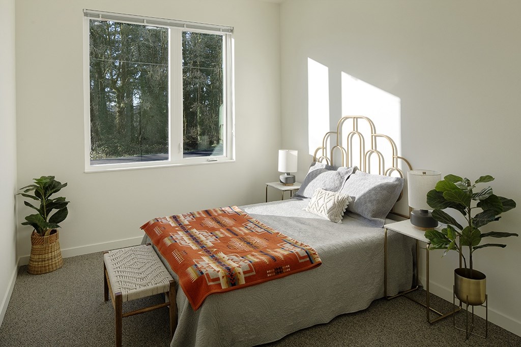 A bedroom with a bed, chair, and potted plants.