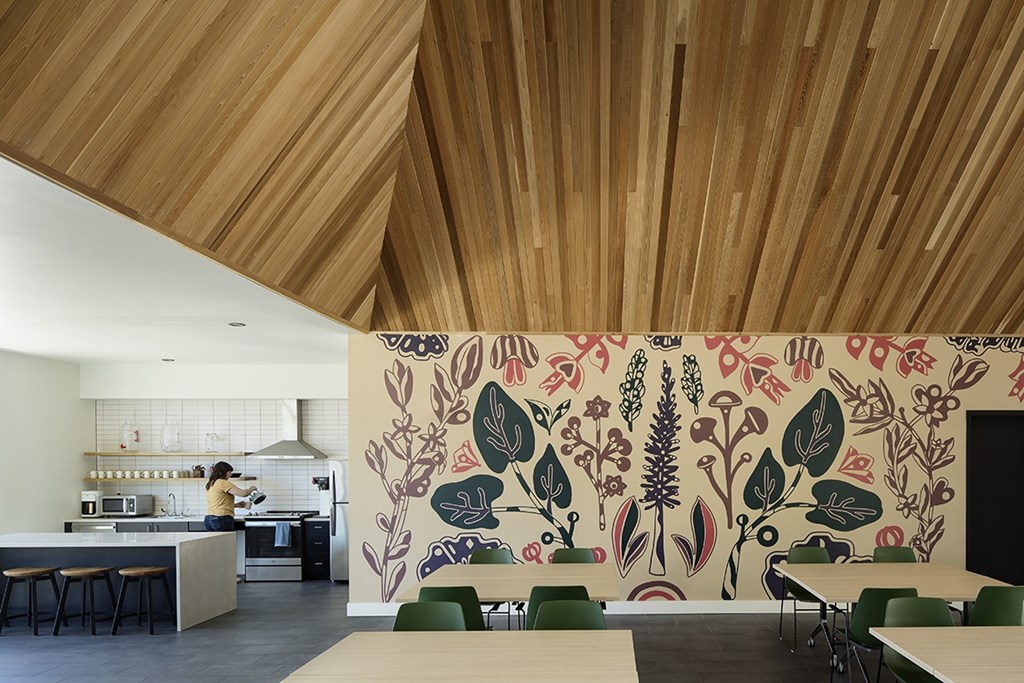 A woman is in a kitchen with a mural of plants on the wall.