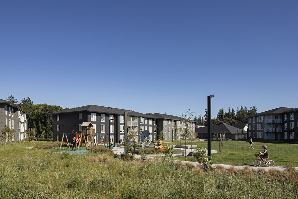 A person is riding a bicycle in a grassy area in front of a building.