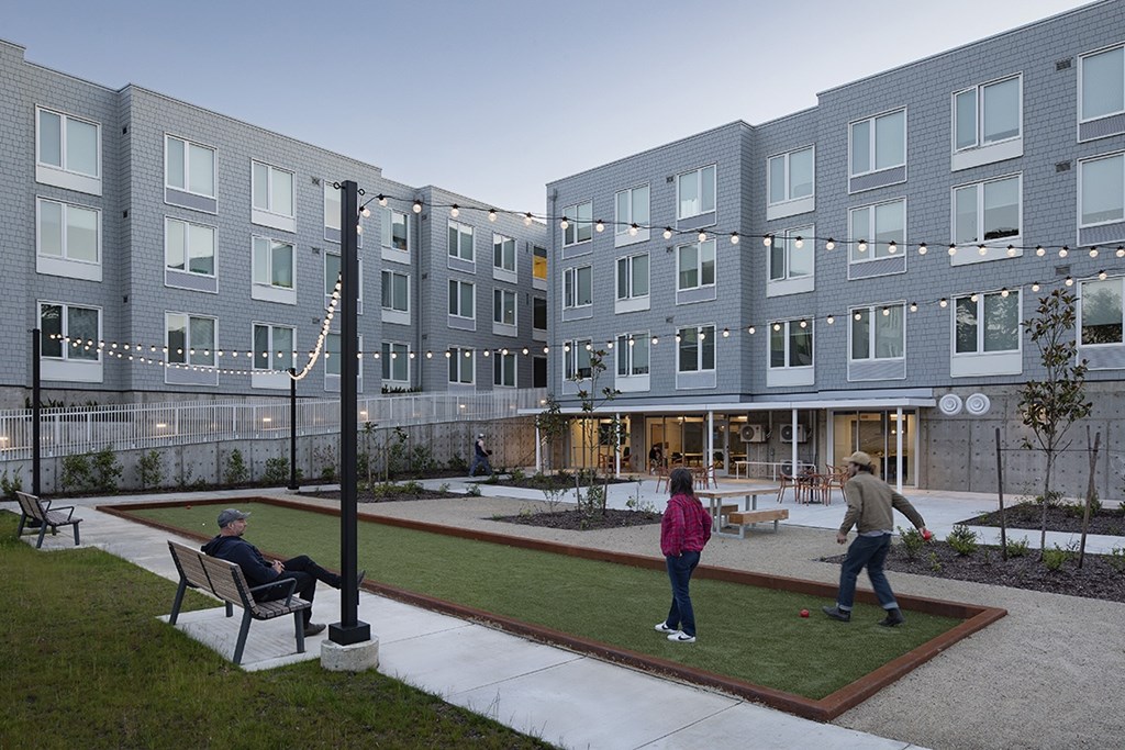 A man is sitting on a bench in a courtyard with a woman and a child playing.
