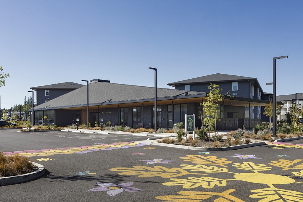 A building with a grey roof and a parking lot with yellow and purple painted flowers in front.