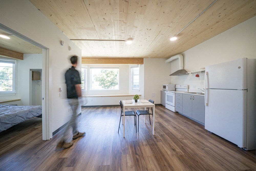 a man walking through a kitchen with a table and a refrigerator