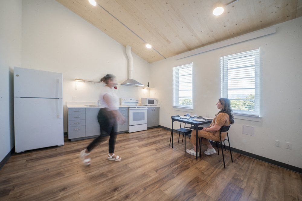 a living room and kitchen with a woman sitting at a table