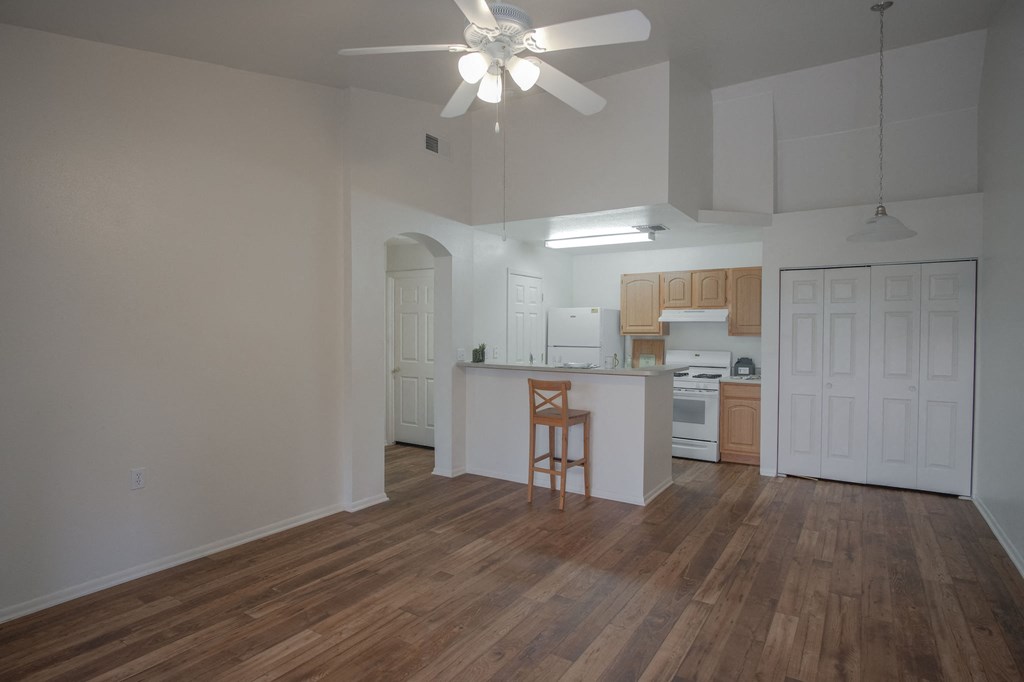 an empty living room with a kitchen and a ceiling fan