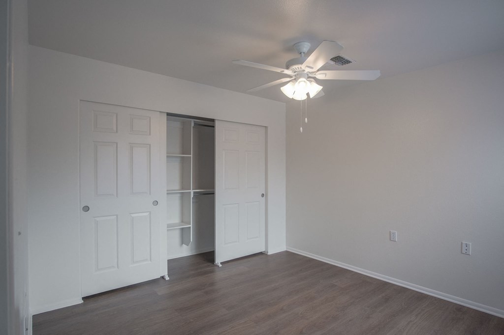 an empty bedroom with fan and closet