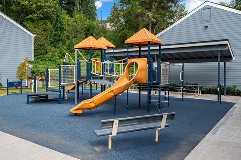 a playground with a slide and benches in front of a building