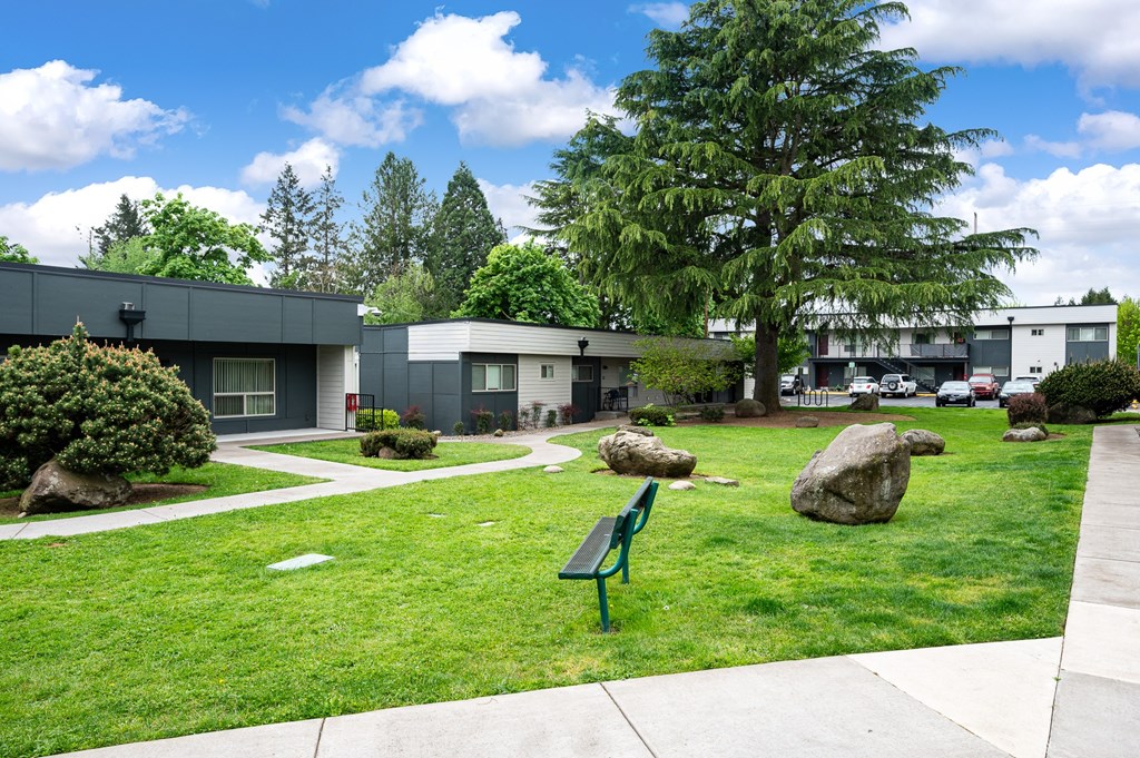 A park with a bench and a few rocks in the foreground and a building in the background.
