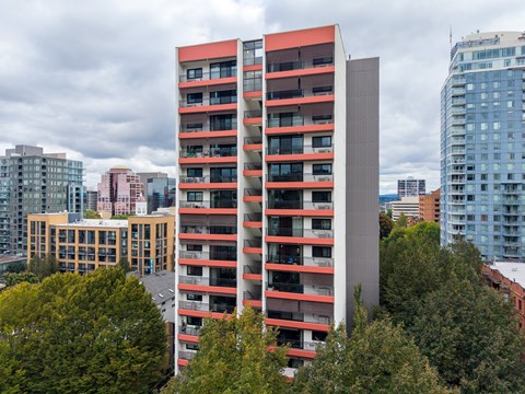 A tall red and grey building stands in front of a row of trees.