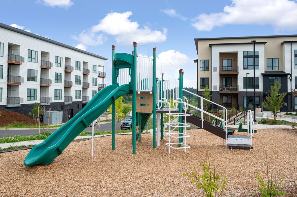 A playground with a green slide and a brown sandy area.