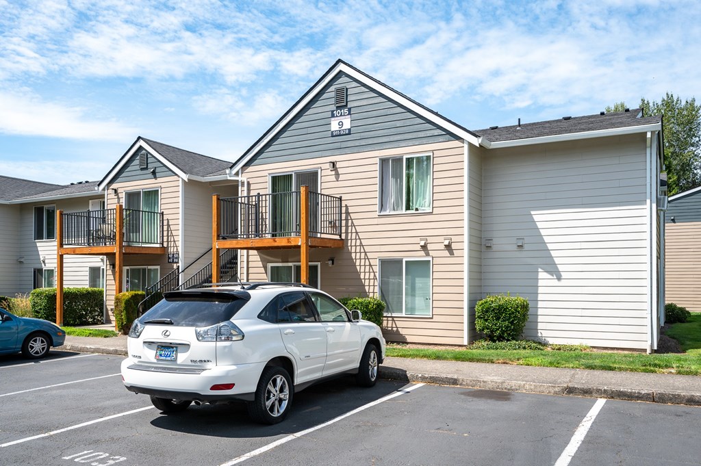 A white car is parked in a parking lot in front of a two-story apartment building.