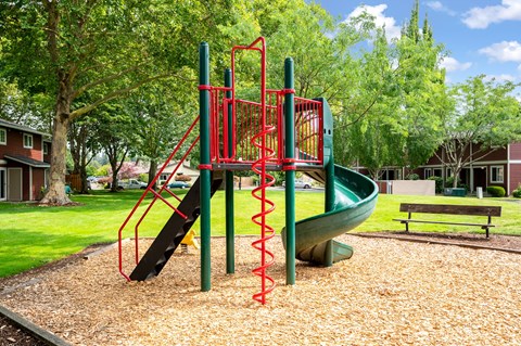 A playground with a red and green slide and a brown bench.