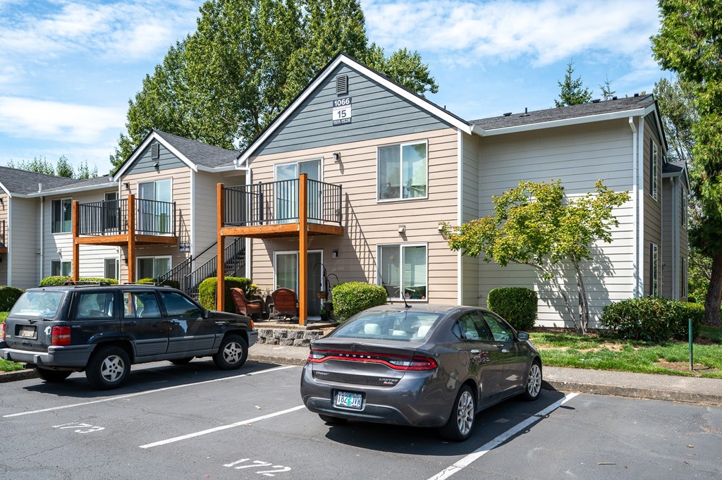 A car is parked in a parking lot in front of a two-story house.