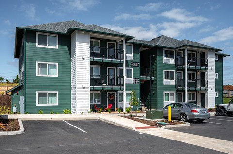 A green and white apartment building with a car parked in front.