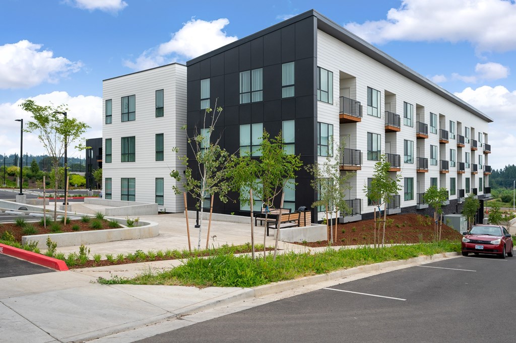A modern apartment building with a red car driving by.