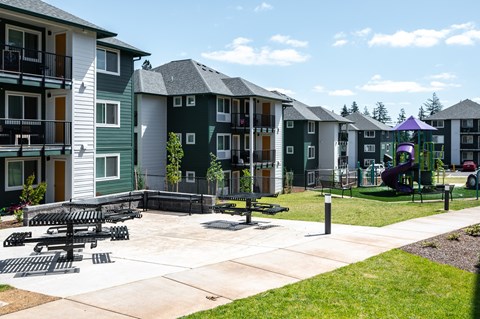 A playground area with a slide and a purple canopy is surrounded by apartment buildings.
