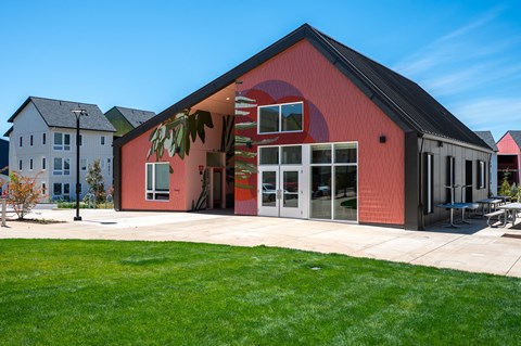 a red house with a patio in front of a green lawn and a blue sky