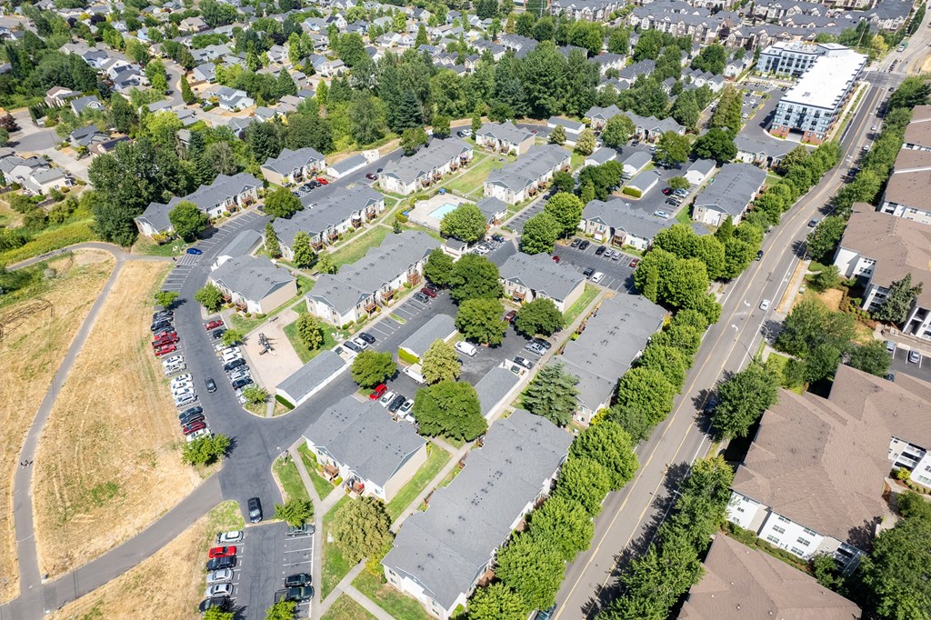 A bird's eye view of a residential area with houses, trees, and a parking lot.