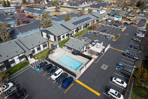 A parking lot with cars and a swimming pool in front of apartment buildings.