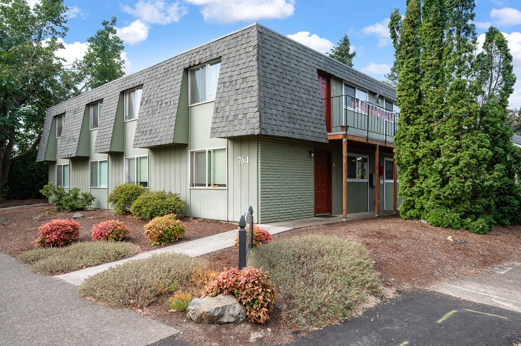 the front of a green apartment building with a sidewalk and landscaping