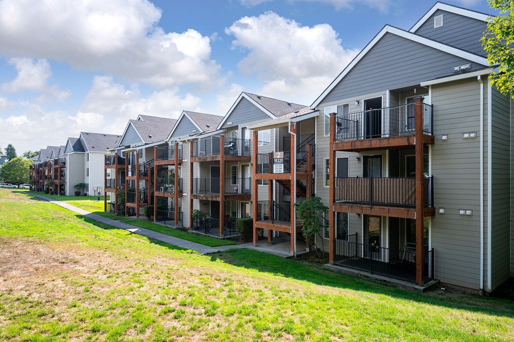 A row of houses with balconies and a green lawn in front.