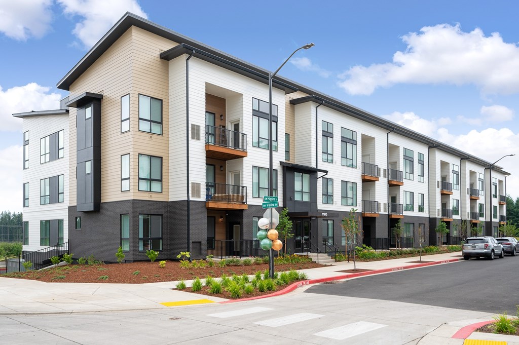 A street view of a modern apartment building with cars parked on the street.