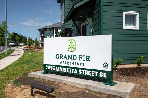 A sign for Grand Fir Apartments is in front of a green building.