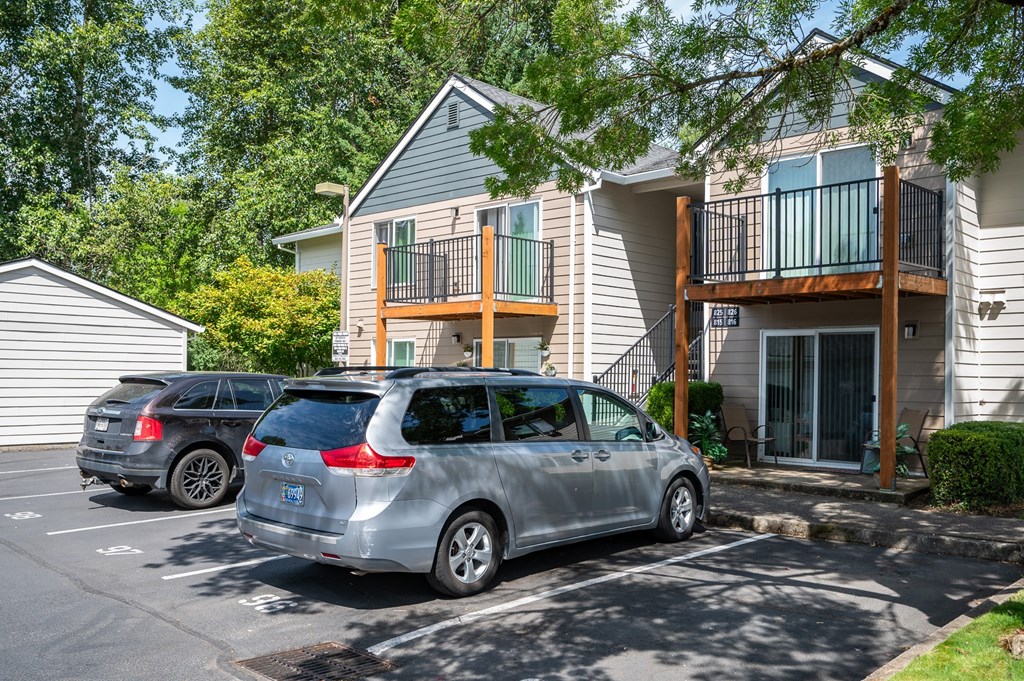 A silver car is parked in a parking lot in front of a two-story apartment building.