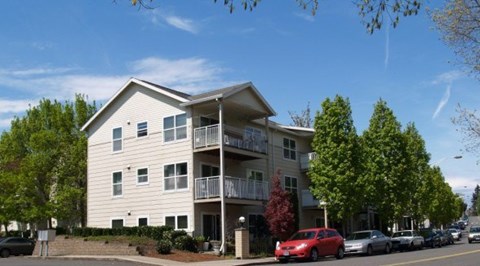 A red car is parked in front of a white apartment building.