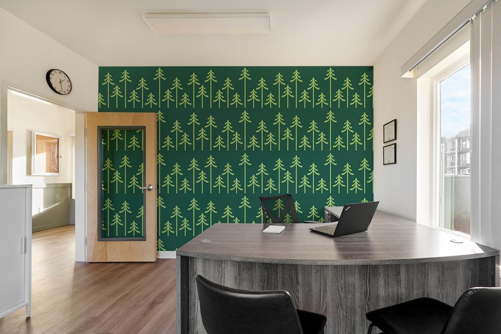 a home office with a desk and a green wall with trees on it