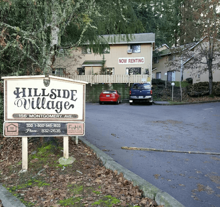 a sign for hillside village with cars parked in front of it