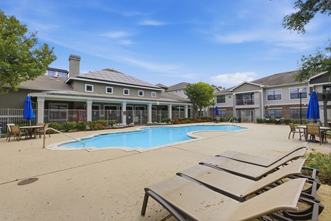 A pool area with sun loungers and a building in the background.
