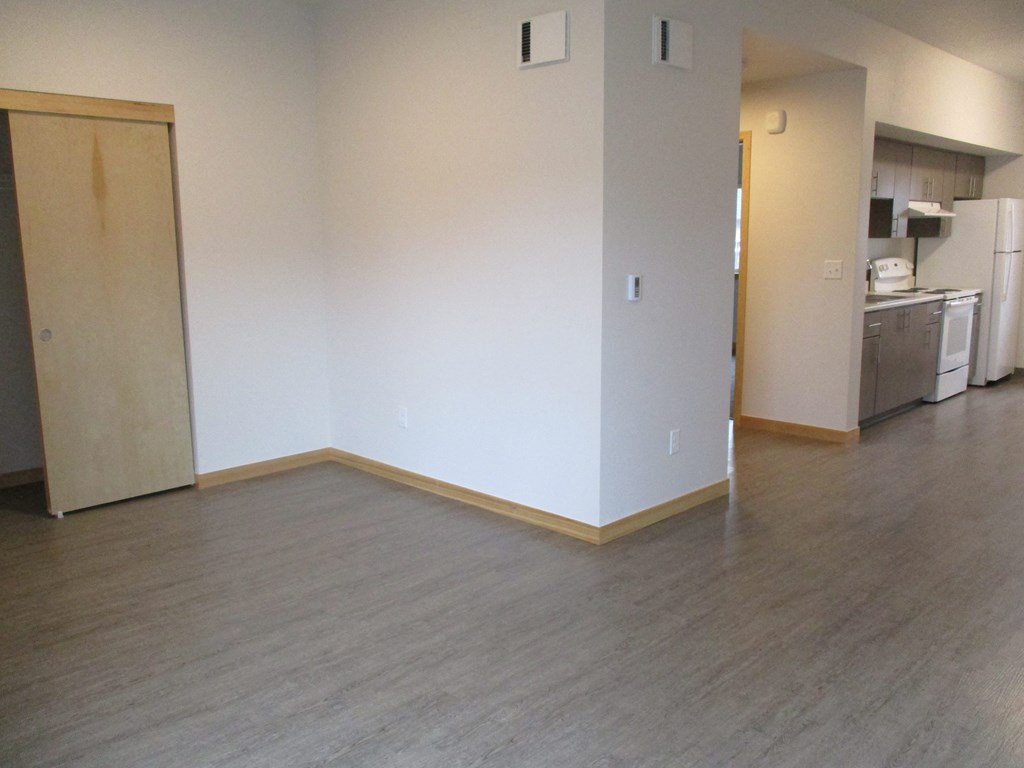 an empty living room with wood floors and a kitchen