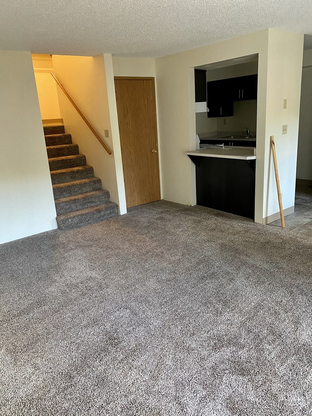 a carpeted living room with a staircase and a kitchen
