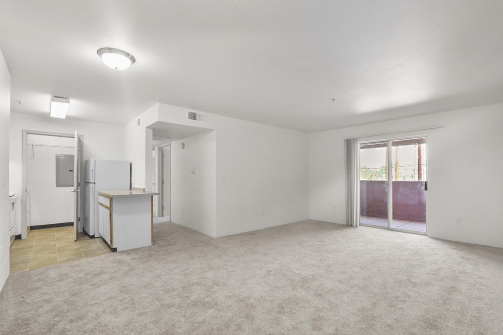 A spacious, empty room with a kitchenette and sliding glass doors.