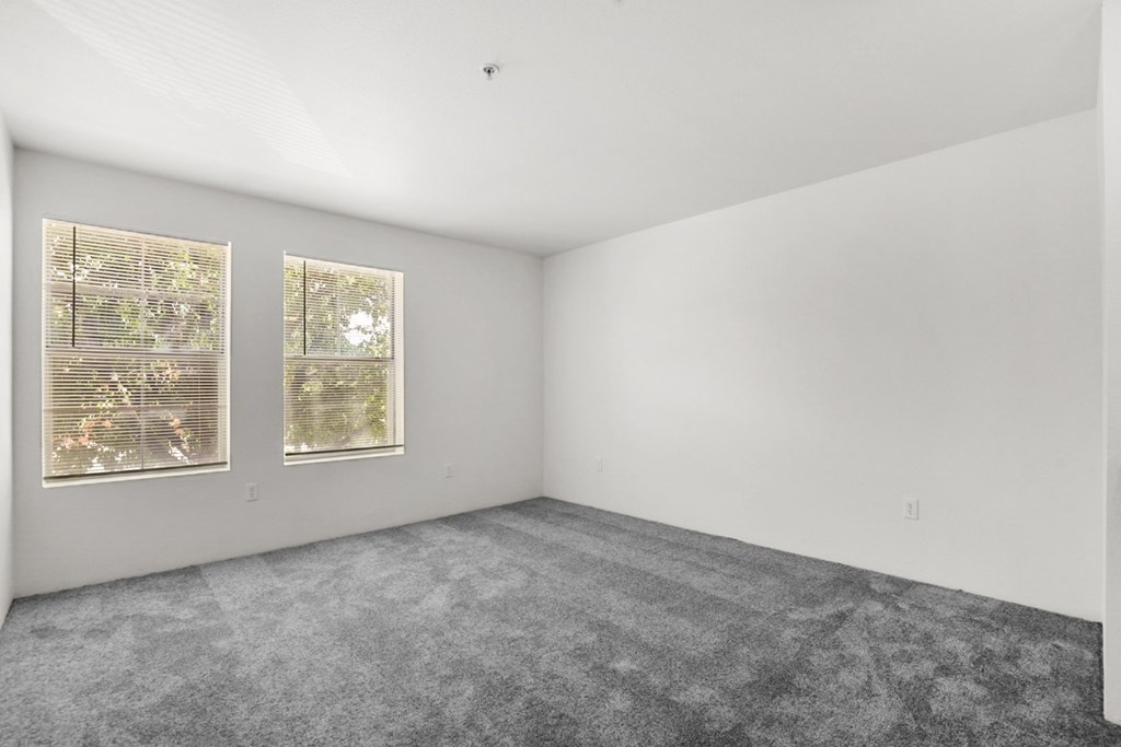 A room with a carpeted floor and two windows.