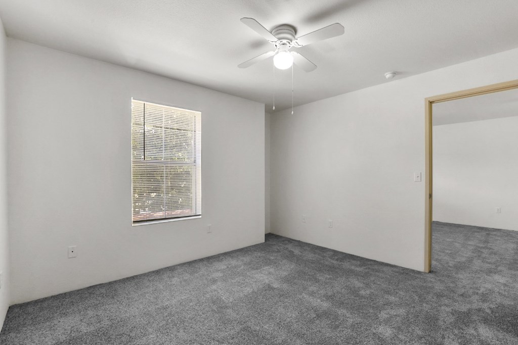 A room with a ceiling fan and a window with blinds.
