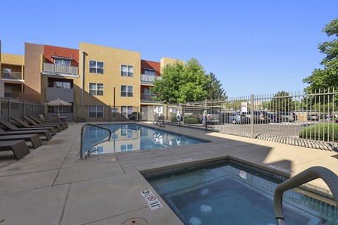 A pool area with a hot tub and lounge chairs in front of apartment buildings.