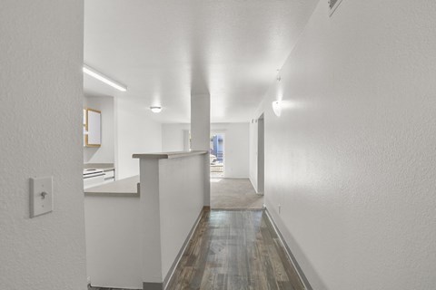 A long hallway with a white wall and a wooden floor.