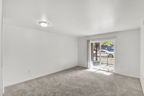 A room with white walls and a carpeted floor with a doorway leading to a balcony.