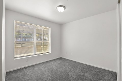 A room with a window and a grey carpet.