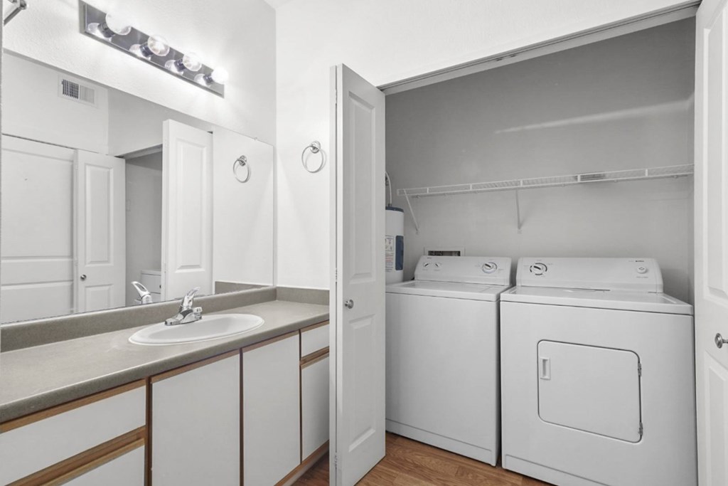 A white bathroom with a sink, mirror, and washer and dryer.