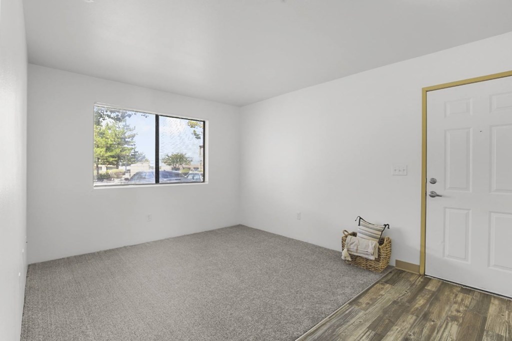 A room with a white door, a window with a view of trees and a fence, and a basket with towels on the floor.